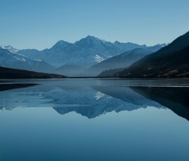 Snow-capped mountains reflected in a calm alpine lake Mountain lake reflecting snow-capped peaks under blue sky